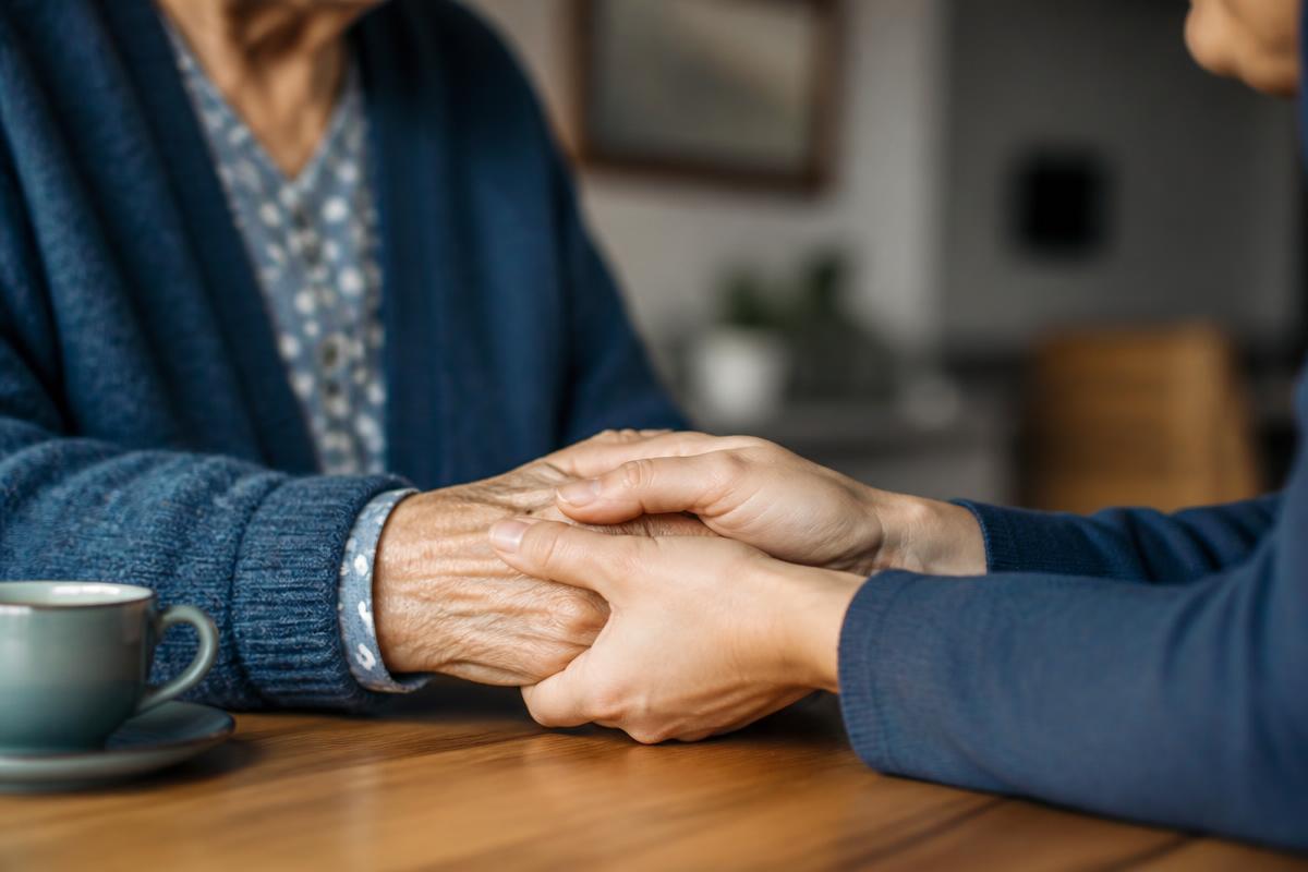 Caregiver gently holding an elderly person's hands at a wooden table